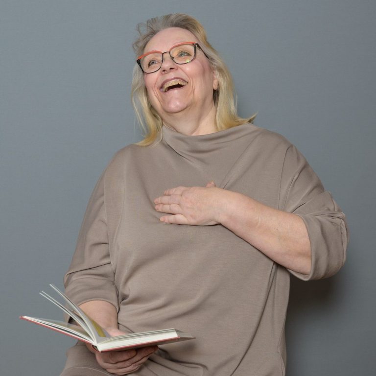 Lächelnde Frau mit Brille, die ein Buch hält und sich erfreut zeigt.